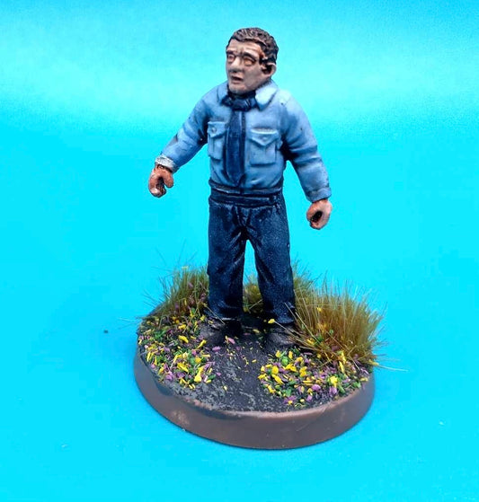 A painted miniature figurine of a man wearing a blue shirt and dark trousers, standing on a round base with grass and small flowers, photographed against a bright blue background.