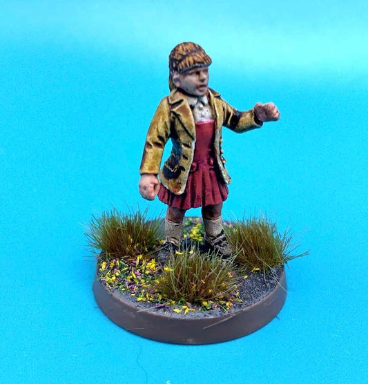 A painted tabletop miniature figurine of a child standing on a round base with grass and small yellow flowers, photographed against a bright blue gradient background.